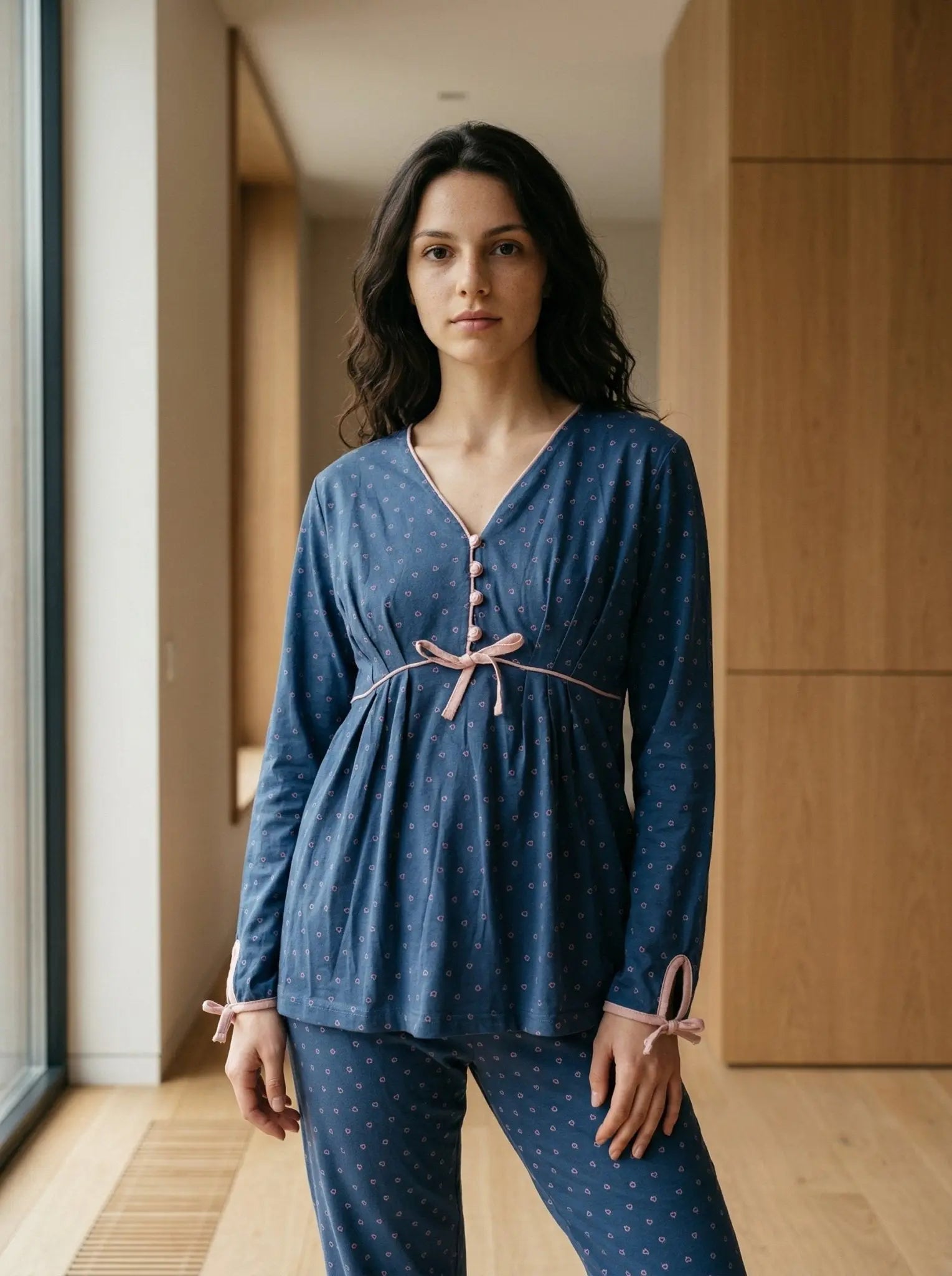Woman wearing a blue pajama set with a bow detail in a room with wooden flooring and walls.