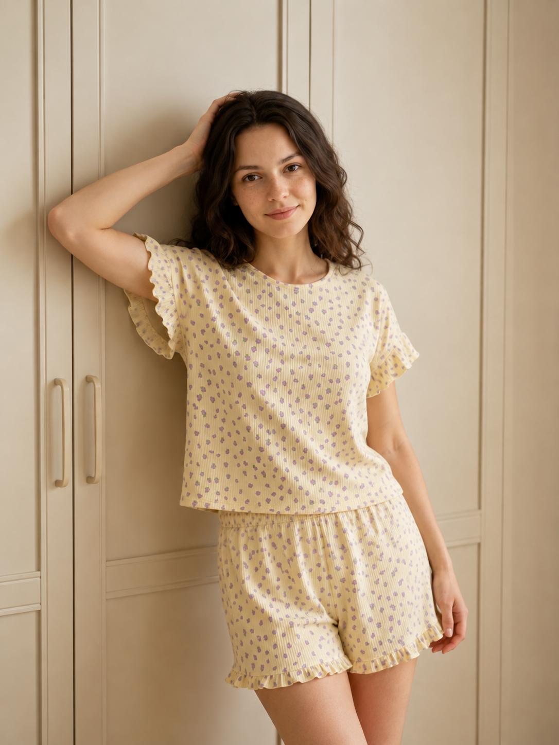 A woman wearing a two-piece pajama set with a small blue floral print on a cream-colored fabric, posing in front of a beige paneled wardrobe.