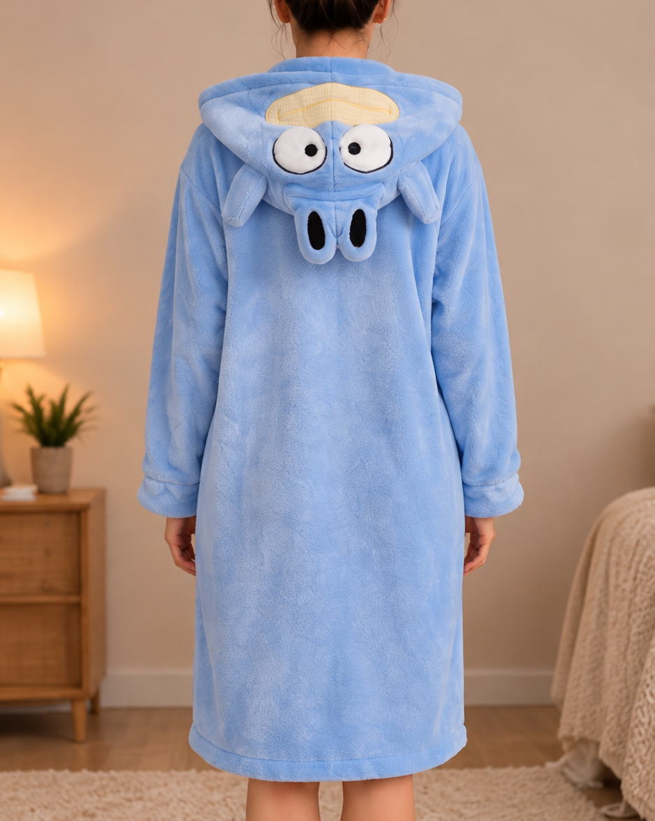 A person standing in a bedroom wearing a light blue plush hooded robe, shown from the back. The robe has a cartoon animal face on the hood with large white eyes, black nose, and a small yellow tuft of hair.